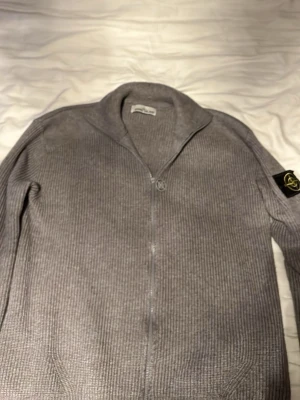 Grå stickad ziptröja från Stone Island - Snygg grå stickad ziptröja från Stone Island med ribbad struktur och stone Island märket på ärmen. Tröjan är i mycket bra skick. Plagget säljs i befintligt skick och enligt bilder/beskrivning. Ingen ångerrätt vid privatförsäljning. Vid frågor – skriv gärna innan köp så undviker vi missförstånd.