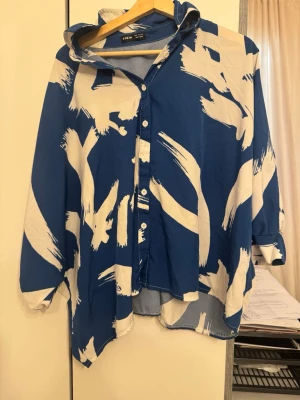 Blåvit oversize skjorta med matchade byxor.  från SHEIN - Snygg oversize skjorta med matchade byxor. från SHEIN i blått med vita abstrakta penseldrag. Skjortan har knäppning framtill, klassisk krage och långa ärmar. Perfekt för en trendig och avslappnad look.