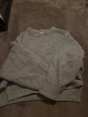 Grå stickad tröja med rund hals - Mysig grå stickad tröja med rund hals och långa ärmar. Tröjan har en enkel och avslappnad passform, perfekt för lager-på-lager och chill dagar. Stickad i ett mjukt material som känns skönt mot huden.