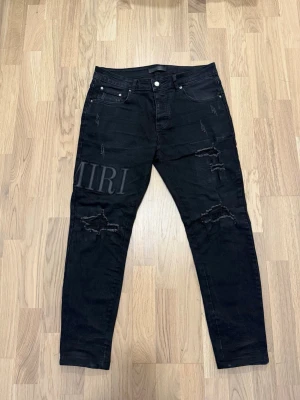 Amiri Jeans - Säljer ett par svarta jeans med slitningar och tryckt logga på vänster lår. Perfekta för dig som gillar streetwear och en edgy stil. inte använd mycket, bara några gånger. Jag är 170cm och 72kg och ni kan se hur den sitter på mig samt finns bild på måtten.