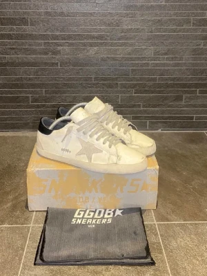 Golden Goose sneakers - Snygga vita sneakers från Golden Goose med ikonisk stjärndetalj på sidan och svarta detaljer vid hälen. Skorna har haft lite slitningar på sulan men blivit tagen till en skomakare, kom gärna med bud!