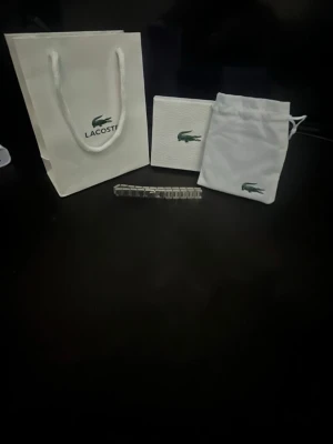 Silverfärgad klocka från Lacoste - Stilren klocka från Lacoste i silverfärgat metallarmband. Kommer med originalförpackning, tygpåse och presentpåse med klassiska Lacoste-loggan. Perfekt accessoar för dig som gillar en clean och tidlös look.