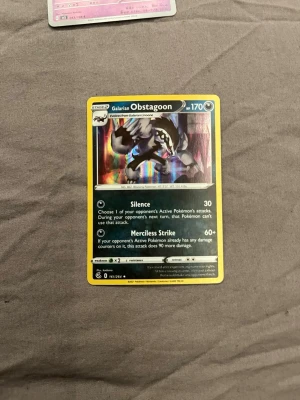 Pokémonkort Galarian Obstagoon - Säljer ett Pokémonkort med Galarian Obstagoon, holografisk design med svart, vitt och regnbågsskimrande detaljer. Kortet har 170 HP och attacker som Silence och Merciless Strike. Perfekt för samlare eller Pokémon TCG-spelare.