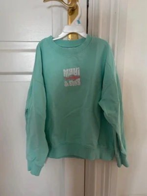 Turkos sweatshirt från Maui & Sons - Cool turkos sweatshirt från Zara med tryckt logga på bröstet. Tröjan har rund halsringning, ribbade muddar vid ärmslut och nederkant samt en avslappnad passform. Perfekt för en chill och avslappnad stil.