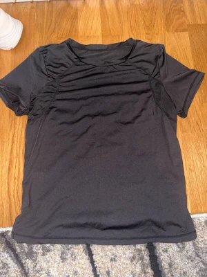 Svart tränings-tshirt - En svart tränings-tshirt med korta ärmar och rund hals. Materialet är lätt och andas, perfekt för gymmet eller löpning. Snygg och enkel design som passar till de flesta sportaktiviteter.