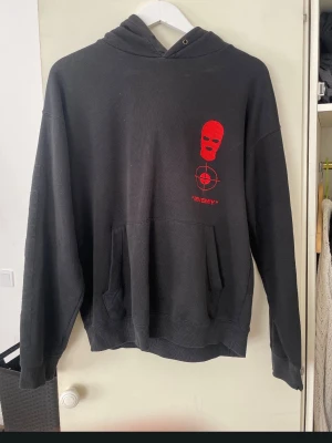 Svart hoodie Black Squad ENEMIES - Svart hoodie från Black Squad med röd skimask och text på bröstet samt stor print på ryggen med en hund och texten ENEMIES i rött. Hoodien har känguruficka och ribbade muddar. Materialet är mjukt och bekvämt, köpt för 57 dollar i USA💓Hoddien är använd ett fåtal gånger💓