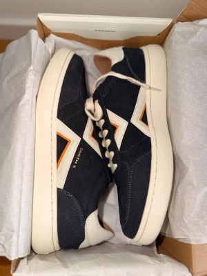 Smith X  - Stilrena sneakers från Smith X i mörkblå mocka med vita och orange detaljer. Skorna har en låg profil, vita snören och en tjock vit sula. Perfekta för dig som gillar en clean och modern look med en twist.