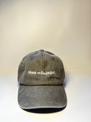 Keps ”hata måndagar” svart  - Den där känslan när väckarklockan ringer och själen lämnar kroppen. “Hata måndagar” är kepsen för dig som inte ens låtsas gilla starten på veckan.  Tillverkad i 100% ekologisk bomull så du åtminstone har det skönt när resten suger.