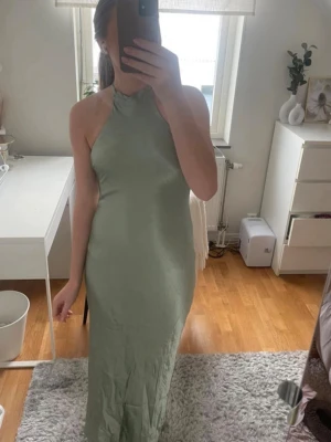 Ljusgrön långklänning/ balklänning  - Säljer en elegant ljusgrön långklänning med halterneck och figurnära passform. Klänningen har en slät, minimalistisk design utan ärmar och är tillverkad i ett glansigt material som ger en lyxig känsla. Perfekt för dig som vill sticka ut med stil. Passar även till bal eller festligare arrangemang. Aldrig använd, helt ny med prislapp. 