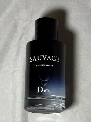 Dior Sauvage Eau de Parfum - Dior Sauvage Eau de Parfum i en elegant mörkblå glasflaska med vit text och svart lock. Flaskan har en stilren, rund form och känns lyxig och modern. Perfekt för dig som gillar exklusiva dofter med en maskulin touch.