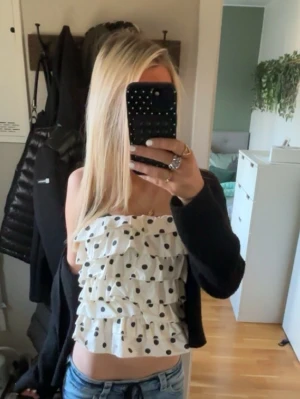 Prickig volangig tubtopp i vitt - Säljer en söt axelbandslös tubtopp i vitt med stora svarta prickar och flera lager volanger. Toppen är croppad och har en luftig passform, perfekt för varma dagar. Supersnygg till jeans eller kjol för en trendig look. Den har en dragkedja baktill. / Den är köpt på plick och vet inte märket men den är som ny. 💕💕