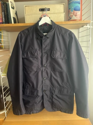 Field Jacket från Fay - Säljer en stilren mörkblå jacka från Fay med knappar och dragkedja. Perfekt för höst och vår då jackan är tun och vattenavvisande!! Jackan har tyvärr tappat två knappar som visas på bilder där en knapp följer med, inget som påverkar jackan när man använder den. Fay är ett grymt italienskt märke som jämförs med herno, hetrego o Moorer. Deras jackor kostar runt 8000kr nya 