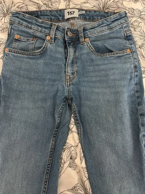 Ljusblå raka jeans från Lager 157 - Säljer ett par korta flare ljusblå jeans från 157 med klassisk femficksmodell. Jeansen har orangea sömmar och silverfärgade nitar. Tillverkade i denim med en snygg tvätt som ger en avslappnad look. Perfekta till vardags för en enkel och stilren outfit.