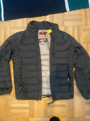 Grön pufferjacka från Parajumpers - Säljer en grön pufferjacka från Parajumpers med gul detalj vid kragen och broderade märkesloggor på insidan. Jackan är superlätt, har dragkedja framtill och två sidofickor med dragkedja. Insidan är ljusgrå och materialet är syntetiskt för en sportig look.
