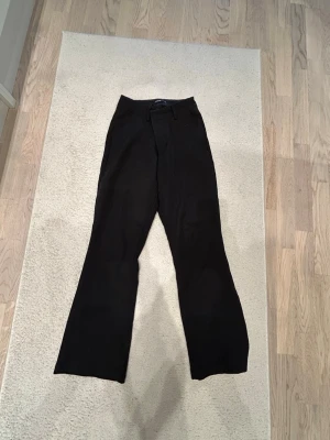 Svarta utsvängda kostymbyxor - Säljer ett par svarta kostymbyxor med utsvängda ben och hög midja. Byxorna har bälteshällor och stängs med knapp och dragkedja. Klassisk och stilren modell som passar till många olika looks.