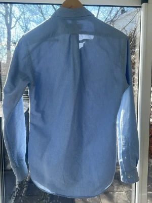 Ljusblå skjorta från Ralph Lauren - Klassisk ljusblå skjorta från Ralph Lauren med button-down krage och broderad logga på bröstet. Skjortan har långa ärmar, knappar framtill och är tillverkad i mjuk bomull. Perfekt för en clean och stilren look.