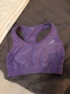Lila sport-bh från Gymshark - Säljer en lila sport-bh från Gymshark med brottarrygg och ventilerande meshdetaljer. Perfekt för träning och ger bra stöd. Stretchigt material som sitter skönt och följer kroppen. Gymshark-logga framtill. Storlek S