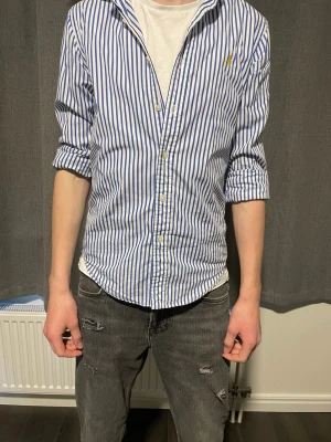 Ralph lauer skjorta - Säljer en klassisk blåvit randig skjorta från Ralph Lauren med knappstängning och den ikoniska loggan broderad på bröstet. Skjortan är i storlek xs men passar även S/M beroende på vikt. Bara höra av dig vid minsta lilla fundering!🙌