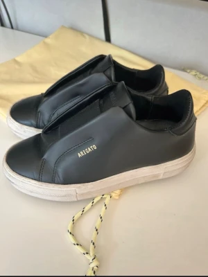 Svarta Axel Arigato sneakers - Stilrena svarta sneakers från Axel Arigato i slät läder med diskret guldfärgad logga på sidan. Säljer pga för stora för mig, de är i storlek 35 men skulle säga att det ör stora i storlek. 