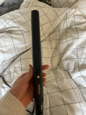 Svart plattång från BaByliss - Säljer en svart plattång från BaByliss med smala, guldfärgade plattor. Plattången har en slimmad design och en sladd som roterar vid fästet för smidig användning. Perfekt för att styla håret rakt eller skapa lockar.