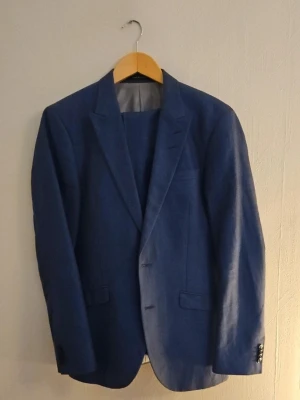 Blå kavaj i linne från Tiger of Sweden - Snygg blå kavaj i klassisk modell med två knappar framtill och fickor med lock. Kavajen har smala slag och är tillverkad i linne, vilket ger en stilren och tidlös look. Perfekt för dig som vill ha en enkel men elegant outfit.