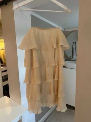 Ljusgul volangklänning med tunna axelband - Säljer en superfin ljusgul klänning med flera lager volanger och tunna axelband. Klänningen har en luftig och flowy känsla, perfekt för varma dagar. Plisserat tyg ger extra struktur och stil. Passar dig som gillar romantiska och boho-vibbar.