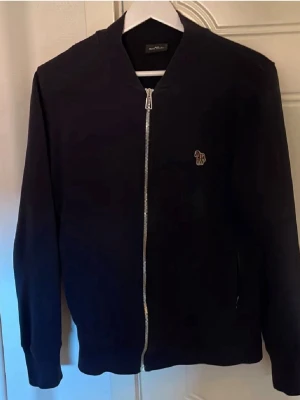 ziptröja från Paul Smith - Snygg svart ziptröja från Paul Smith med silverfärgad dragkedja och diskret logga på bröstet. Tröjan har lång ärm, rak passform och mjukt material som känns skönt mot huden. 