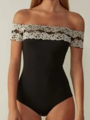 Svart off shoulder body med spets - Snygg svart body med off shoulder-modell och bred spetskant i vitt runt axlarna. Kroppsnära passform och tryckknappar i grenen. Perfekt för dig som gillar en feminin och trendig look. Materialet känns mjukt och stretchigt.