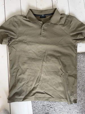 Beige piké från J.Lindeberg - Säljer en stilren beige piké från J.Lindeberg med klassisk krage och knappar framtill. Tillverkad i mjuk bomull och har korta ärmar. Perfekt för dig som gillar en clean och enkel look.