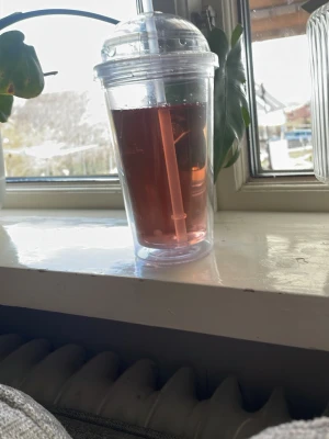 Transparent plastmugg med lock och sugrör - Säljer en transparent plastmugg med tillhörande lock och sugrör. Muggen har en enkel och modern design, perfekt för kalla drycker. Sugröret är också transparent och muggen rymmer en generös mängd vätska.
