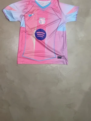 Barça matchtröja rosa/blå Nike - Snygg FC Barcelona matchtröja i rosa och ljusblått med vita och blå detaljer. Tröjan har klubbmärke, Nike-logga och Spotify-logga på bröstet. Tillverkad i lätt och ventilerande material, perfekt för fotbollsträning eller match.