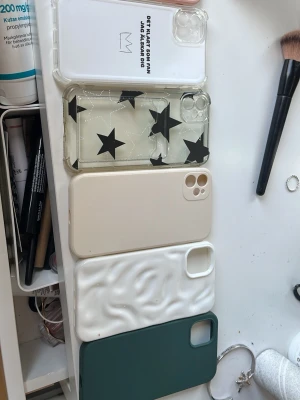 Fem olika mobilskal till iPhone 11 - Säljer fem snygga mobilskal till iPhone 11. Ett transparent med svart text och krona, ett genomskinligt med svarta stjärnor, ett beige, ett vitt med vågig struktur och ett mörkgrönt.  Typ 10-15 kr styck 