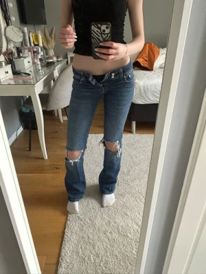 Blå lowwaist jeans med hål vid knäna - Säljer ett par lowwaist bootcut jeans från lager 157 med slitningar på båda knäna. Säljer för att dom inte passar mig. Storlek 32. Dom är väldigt lowwaist och passar nån som är runt 170. Väldigt bra skick!
