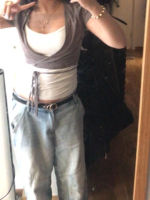 Brun omlottopp med knyt - Säljer en brun omlottopp med knyt i midjan. Toppen har korta ärmar och är croppad, perfekt att styla över ett linne eller topp. Materialet känns mjukt och stretchigt, och färgen är en snygg mörkbrun ton.