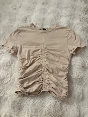 Beige topp från divided H&M - En Beige topp med någon typ av scrunch både bak, fram och på sidorna vilket ger en tajt effekt. Storlek XS men är lite kortare och mindre än de. Bara använd någon gång