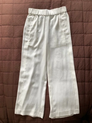 Vita byxor - H&M - Vita vida byxor från H&M, resår i midjan. Detalj på sidan, se bild. Storlek 32. Längd: ca 87cm. Innerbenslängd: ca 57cm. Endast använda ett fåtal gånger - i mycket fint skick 🌸