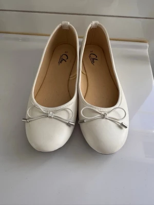 Vita ballerinaskor med rosett - Snygga vita ballerinaskor med rund tå och dekorativ rosett framtill. Använda ungefär 2 gånger och är normala i storleken.