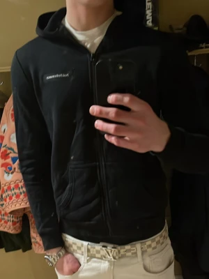 Svart hoodie från Peak Performance - Säljer en svart hoodie från Peak Performance med dragkedja framtill och fickor på sidorna. Hoodien har en liten logga på bröstet och är tillverkad i mjukt bomullsmaterial. Perfekt för en avslappnad och stilren look. Den är för liten för mig vilket syns men den är M 170/92A