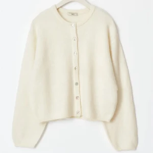 Vit kofta från Gina - Mysig vit kofta från Gina med knappar framtill. Perfekt för kyligare dagar med sin mjuka och bekväma design. Långärmad och enkel att matcha med olika outfits.