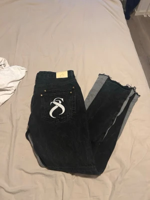 Svarta jeans från Sterlingz med råa kanter - Säljer ett par svarta jeans från Sterlingz med vit logga på bakfickan. Jeansen går lite större vid ben öppningarna är resten av byxorna men det är inte med mycket. Tillverkade i denim. Vet inte riktigt vad storleken men är 188 cm och ni ser hur dem sitter, det är därför det står nån random storlek. Pris kan diskuteras men köpte dem för 850kr så säljer dem för ganska bra pris
