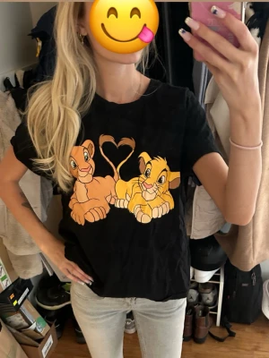Svart Lion King t-shirt New Yorker - Säljer en svart t-shirt från FB Sister med Disney The Lion King-tryck framtill. Motivet visar Simba och Nala med svansarna formade som ett hjärta. T-shirten har normal passform och korta ärmar. Perfekt för dig som älskar Disney och vill ha en unik look.
