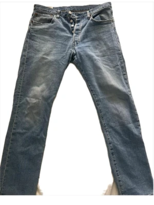 Levi's ljusblå raka jeans - Säljer ett par klassiska ljusblå jeans från Levi's med rak passform och knappgylf. Jeansen har fem fickor och är tillverkade i slitstark denim. Perfekta för en avslappnad och tidlös stil. Klippta längst ner.