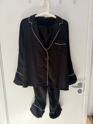 pyjamas från Oysho i storlek L -  pyjamas från Oysho i storlek L. Tvådelat set med skjorta och byxor i mjukt, satinkänsla-material. Klassisk modell med kontrastpasspoal. Oanvänd med mycket fint skick.  Storlek: L