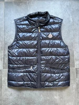 Moncler gui väst  - Tjena, säljer nu denna riktigt snygga och populära Moncler gui västen, den är i bra skick men finns små skador som visas på några av de sista bilderna, dragkedjan är replacment zipper och ena zippen på ena fickan är borta, passar bra på mig som är 180 cm och väger 65 kg, storlek 2 ~ S/M, hör av er vid frågor och funderingar🙌🤝 