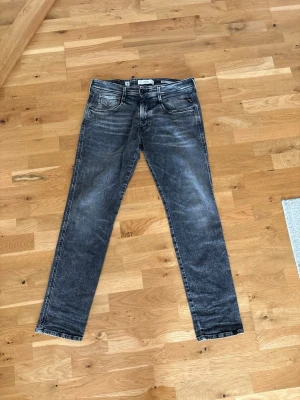 Svarta slim fit jeans från Nudie Jeans - Säljer ett par svarta slim fit jeans från replay med snyggt slitna detaljer och klassisk femficksmodell. Jeansen har en något tvättad look och raka ben. Perfekta för dig som gillar en avslappnad men ändå stilren vibe.