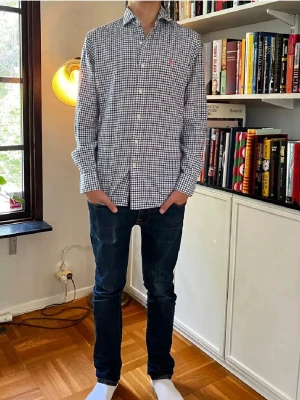 Rutig blå skjorta från Polo Ralph Lauren - Säljer en klassisk långärmad skjorta från Polo Ralph Lauren med rutigt mönster i blått och vitt. Skjortan har knappar hela vägen och en liten broderad logga på bröstet. Perfekt för dig som gillar stilrena plagg med snygga detaljer.