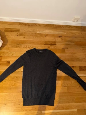 Mörkgrå tröja från Dressmann - Supersnygg mörkgrå tröja från Dressmann i mjuk bomull. Tröjan har rund halsringning, långa ärmar och ribbade muddar vid ärmslut och nederkant. Perfekt att matcha med jeans eller chinos för en clean look.