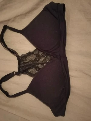 Svart bralette med spetsdetalj - Snygg svart bralette med tunna axelband och dekorativ spets framtill. Mjuk och bekväm modell utan bygel, perfekt för dig som gillar en enkel men ändå stilren look. Spetsen ger en extra touch av elegans.