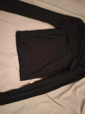 Svart stickad långärmad tröja - En enkel svart stickad tröja med rund hals och långa ärmar. Tröjan har ribbstickade muddar vid ärmslut och nederkant, vilket ger en snygg och klassisk look. Perfekt att matcha med jeans eller kjol för en stilren outfit.