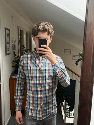 Färgglad rutig skjorta från Ralph Lauren med knappar - Säljer en långärmad skjorta från Ralph Lauren med klassiskt krage och knappar framtill. Skjortan har ett rutigt mönster i blått, grönt, rött, gult och vitt. Perfekt för dig som gillar färg och vill ha en skjorta som sticker ut. Materialet känns som bomull och passformen är normal.